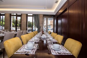 A long dining table set for a meal with yellow chairs, large windows, and a view of the street outside. - An Grand Hotel (Ankara)