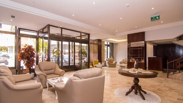 A lobby with beige sofas, a round table, and a large potted plant. - An Grand Hotel (Ankara)