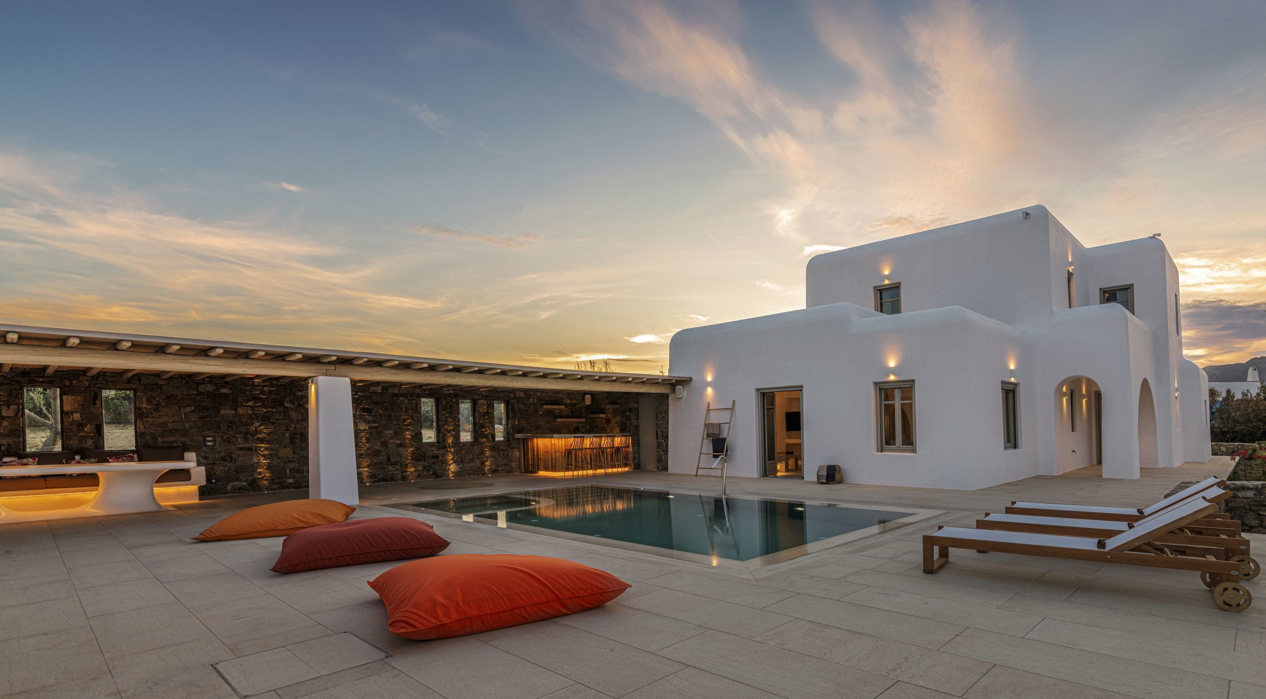Un moderno edificio blanco con piscina, zona de estar exterior y un muro de piedra.