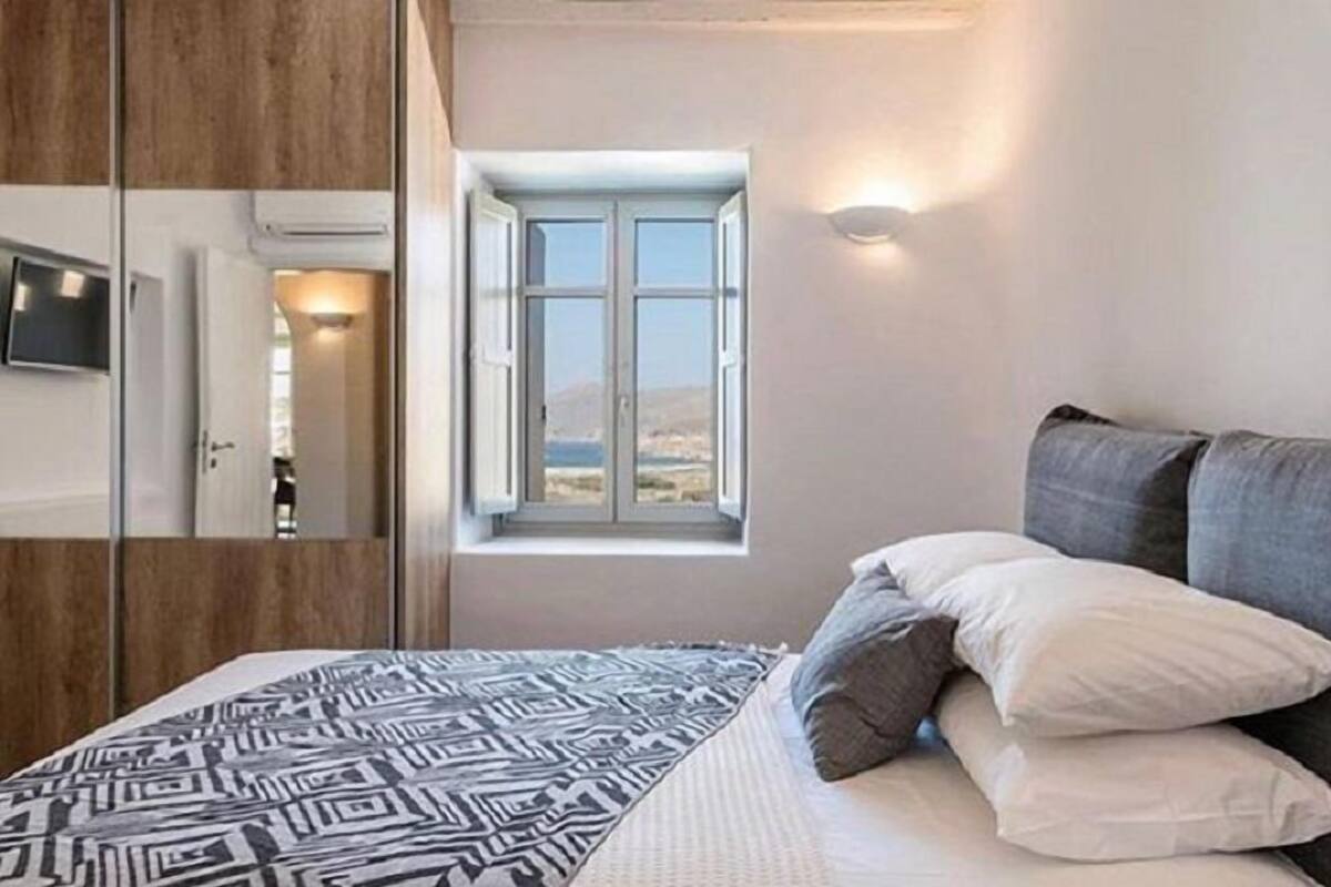 A bedroom with a bed, pillows, a window, and a TV on the wall.