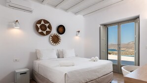 Ein Schlafzimmer mit einem Bett, einem kleinen Nachttisch, einem Mülleimer und Meerblick durch eine Glastür.