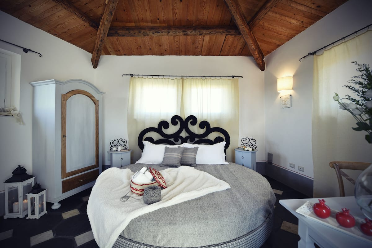 Ein Schlafzimmer mit Holzboden, einem Bett mit weißer Decke, einem Nachttisch mit Lampe, einem Kleiderschrank und einem Fenster mit Vorhängen.