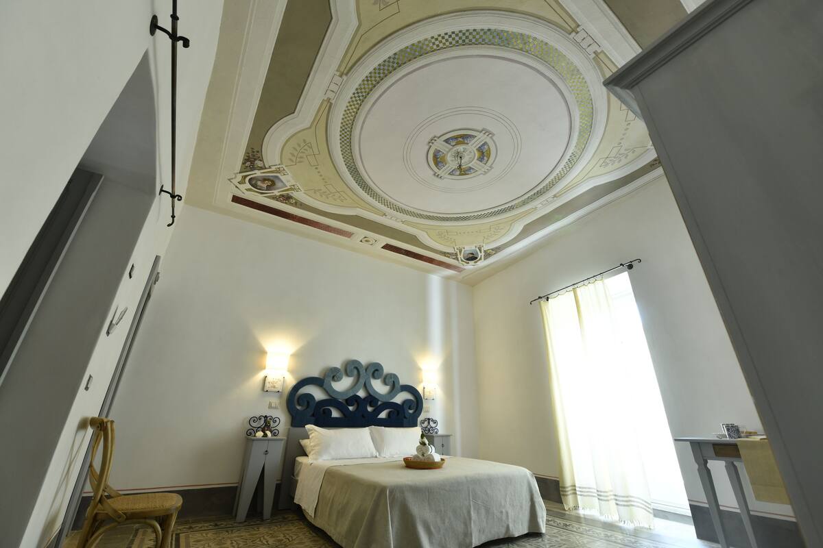Ein Schlafzimmer mit einem großen Bett, einer verzierten Decke und Blick ins Freie.