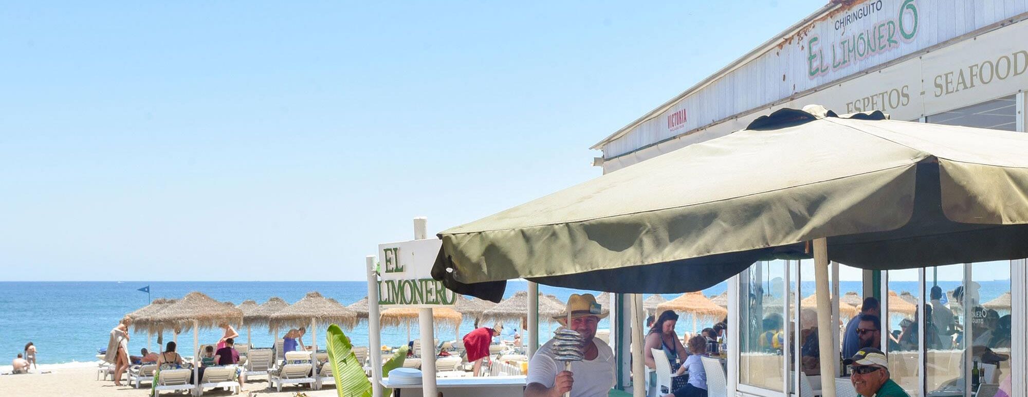 A beachside restaurant with outdoor seating, a sign reading "EL LIMONERO," and thatched umbrellas.
