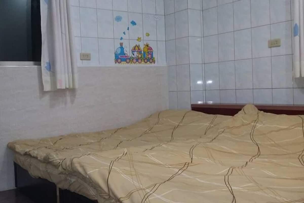 A room with a bed, a window with curtains, and a wall with a children's drawing.