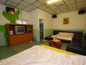 A room with a bed, a sofa, a television on a wooden cabinet, and a painting on the wall.