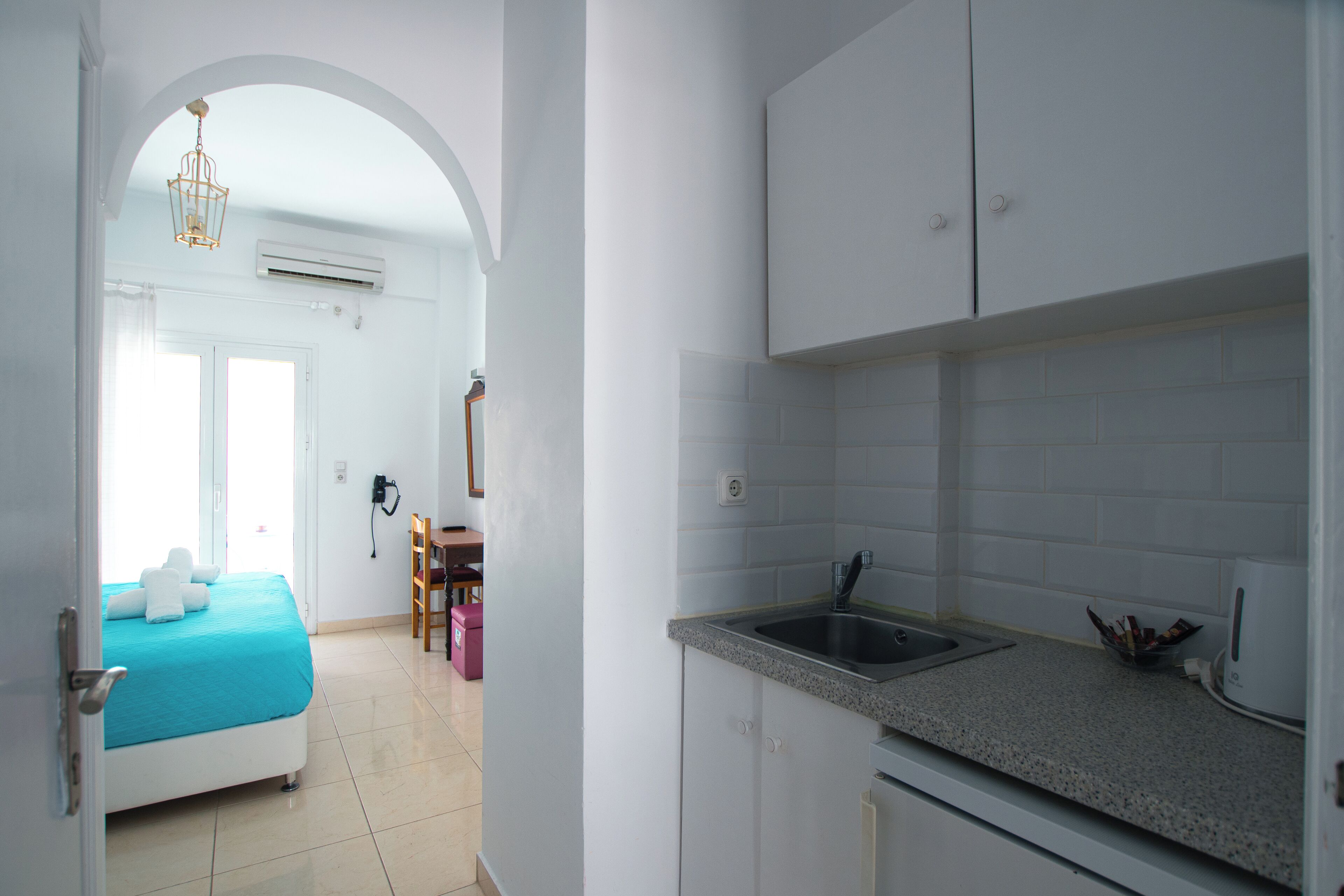 A hotel room with a bed, a kitchenette, and an arched doorway leading to another room.