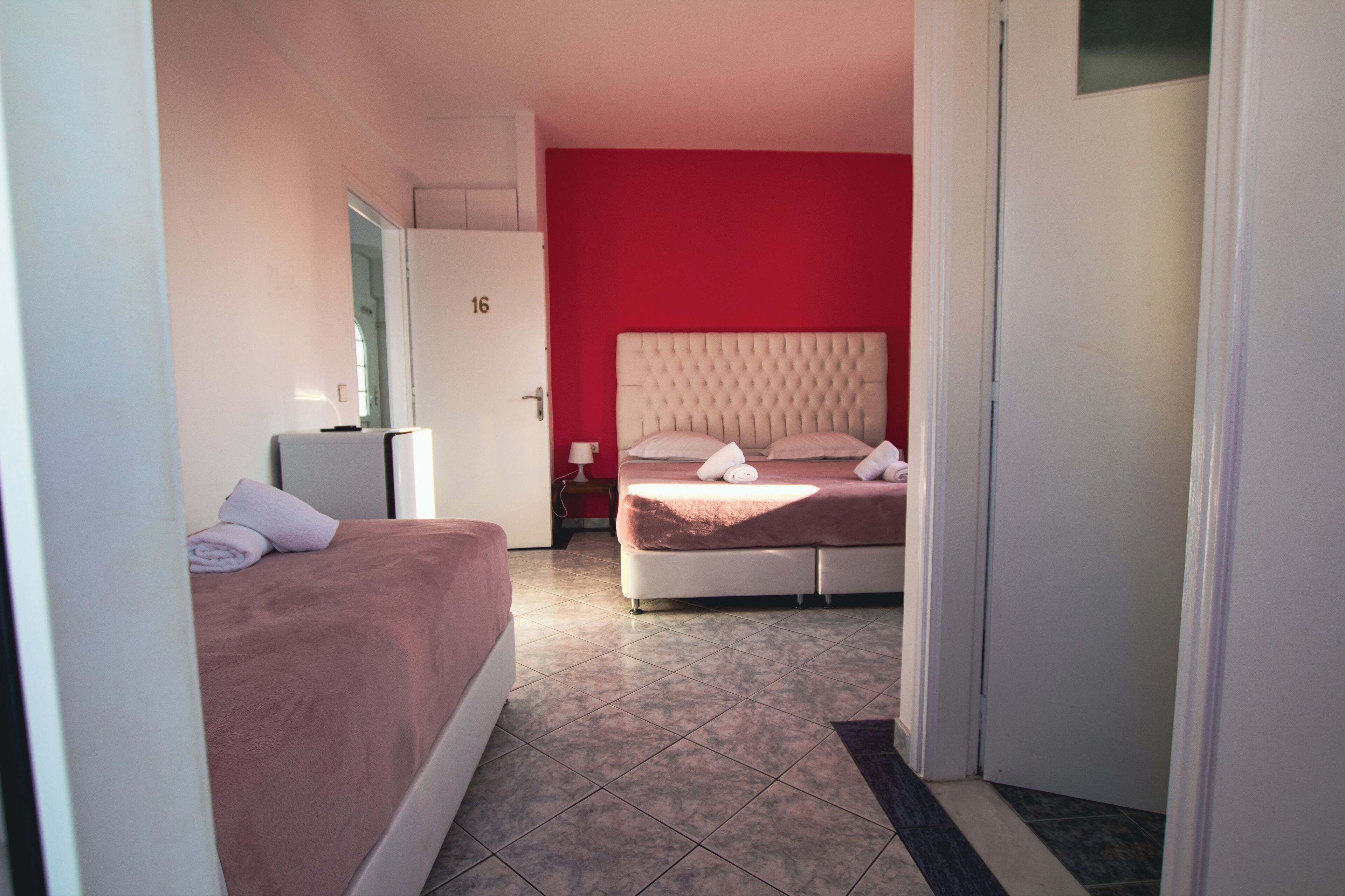A hotel room with a bed, a desk, and a door marked with the number 16.