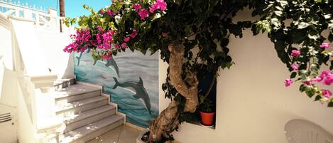 A staircase leading to a balcony with a mural of a dolphin, a tree with pink flowers, and a white chair.