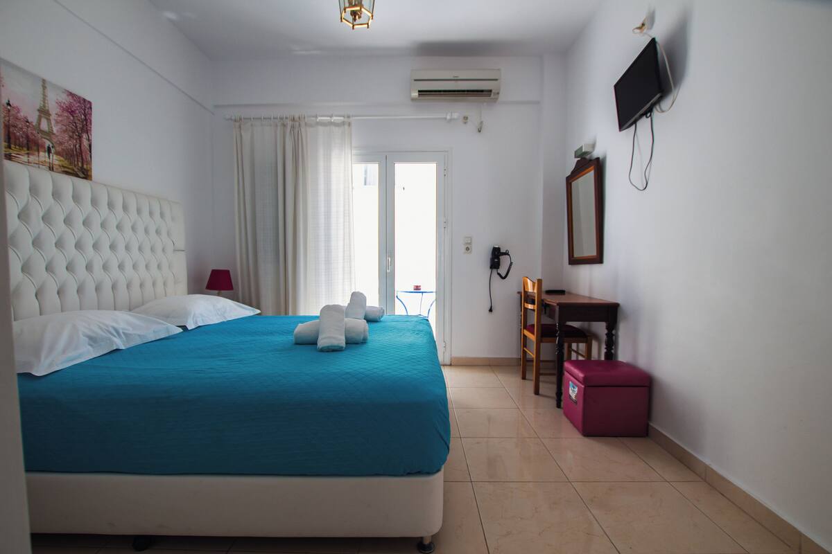 Habitación de hotel con una cama grande, un escritorio, una silla, un televisor y una ventana con cortinas.