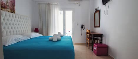 Habitación de hotel con una cama grande, un escritorio, una silla, un televisor y una ventana con cortinas.