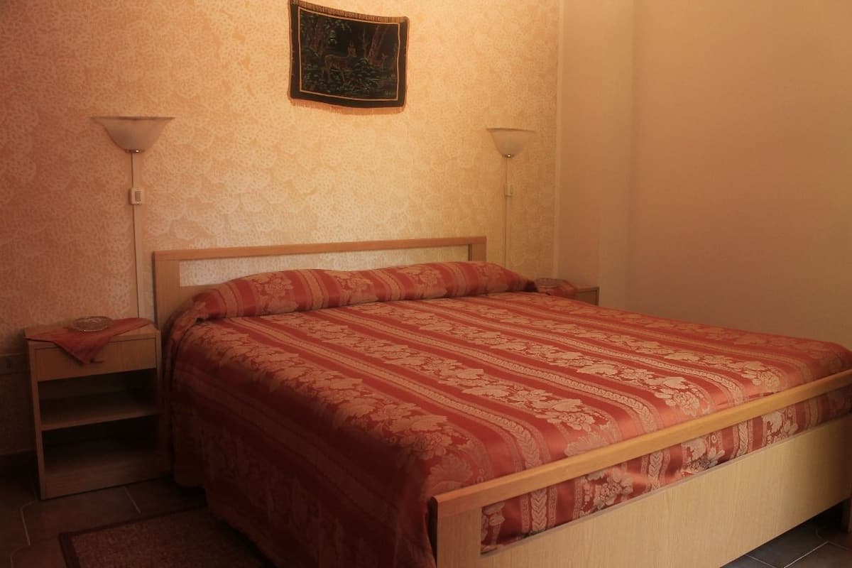Un dormitorio con una cama de madera, una mesita de noche, una lámpara de pared y un cuadro en la pared.