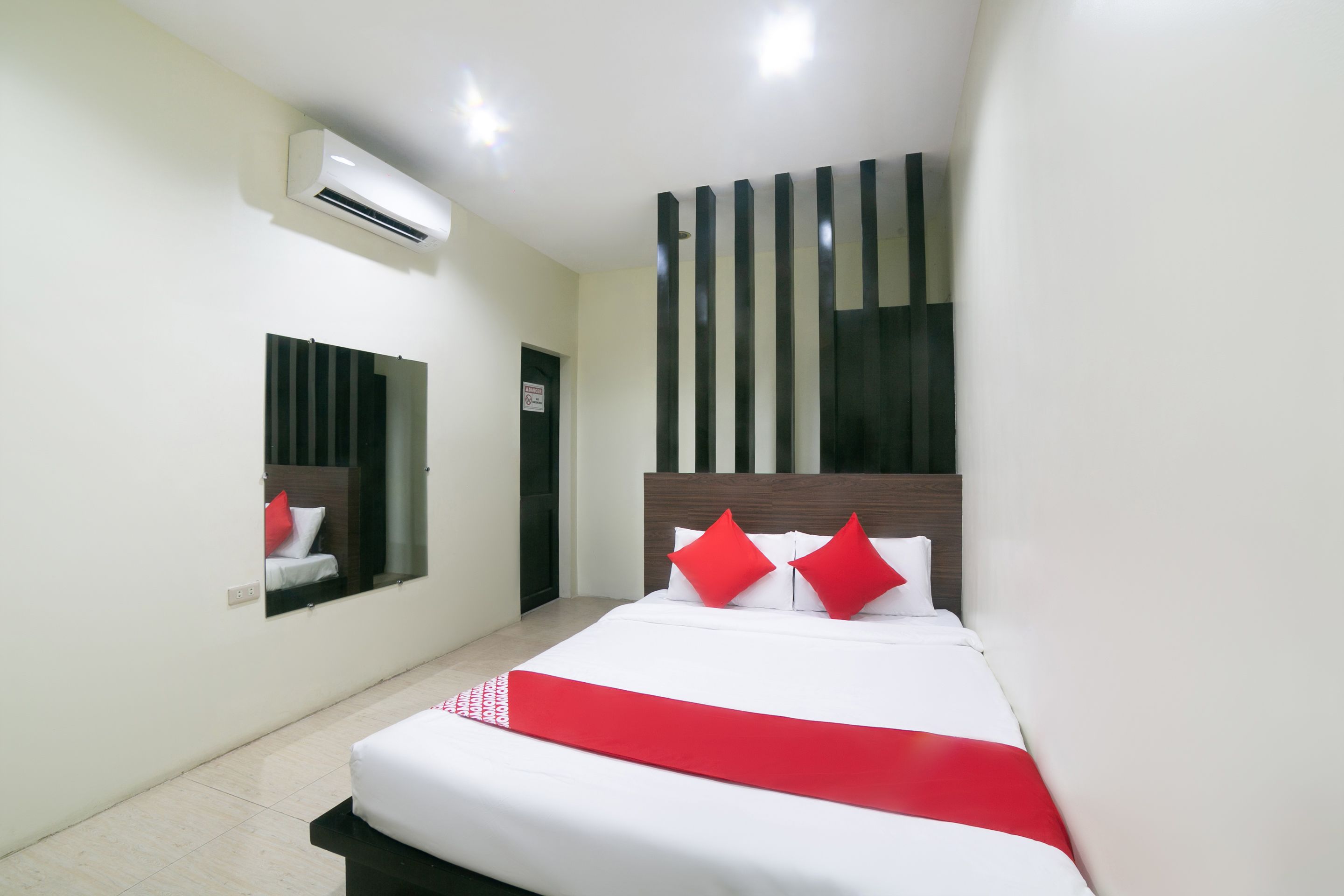 A hotel room with a large bed, a mirror, an air conditioning unit, and a window with vertical blinds.