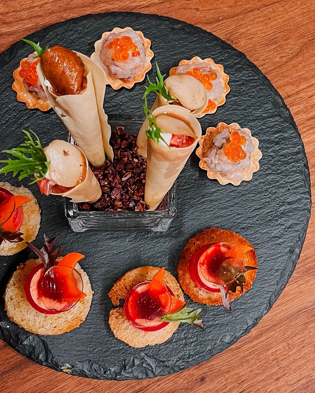 Diversas tapas y aperitivos pequeños dispuestos sobre una tabla de pizarra, con adornos.