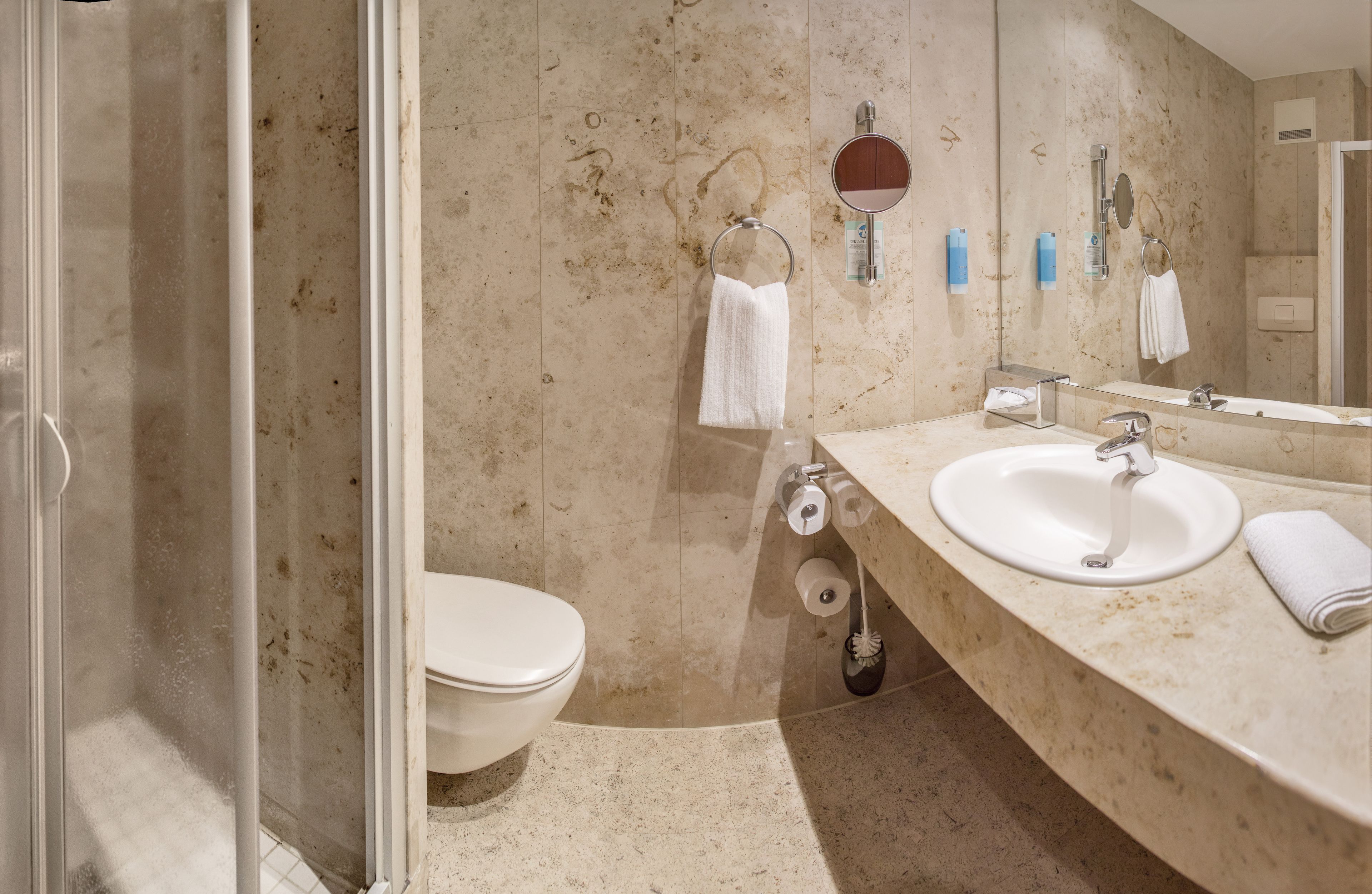 Een badkamer met een toilet, een wastafel, een douche en een spiegel.