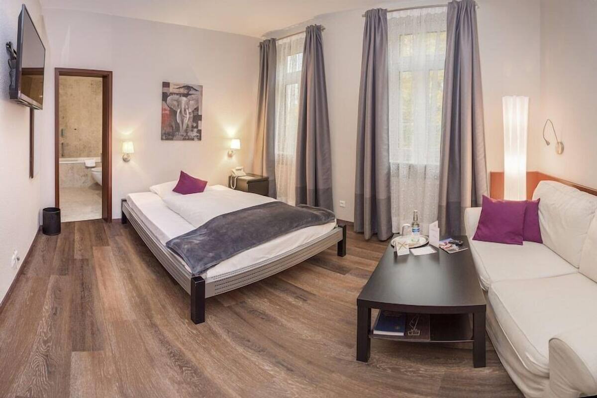 Ein Hotelzimmer mit Bett, Sofa, einem kleinen Tisch, einem Fernseher und Bildern an den Wänden.