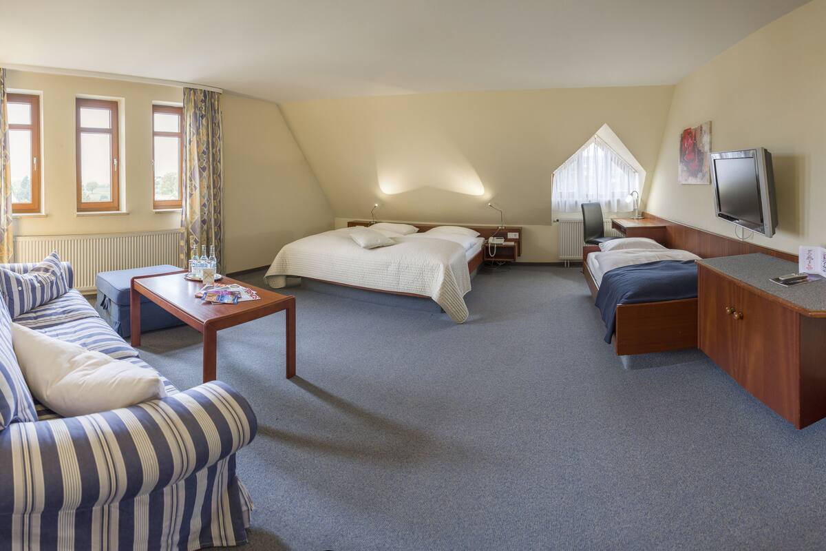 Ein Hotelzimmer mit Bett, Sofa, Schreibtisch, Fernseher und einem Fenster mit Vorhängen.