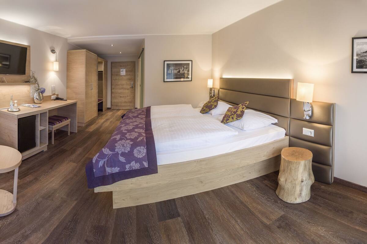 Ein Hotelzimmer mit einem großen Bett, einem Schreibtisch mit Stuhl, einem Fernseher und einem kleinen runden Tisch.