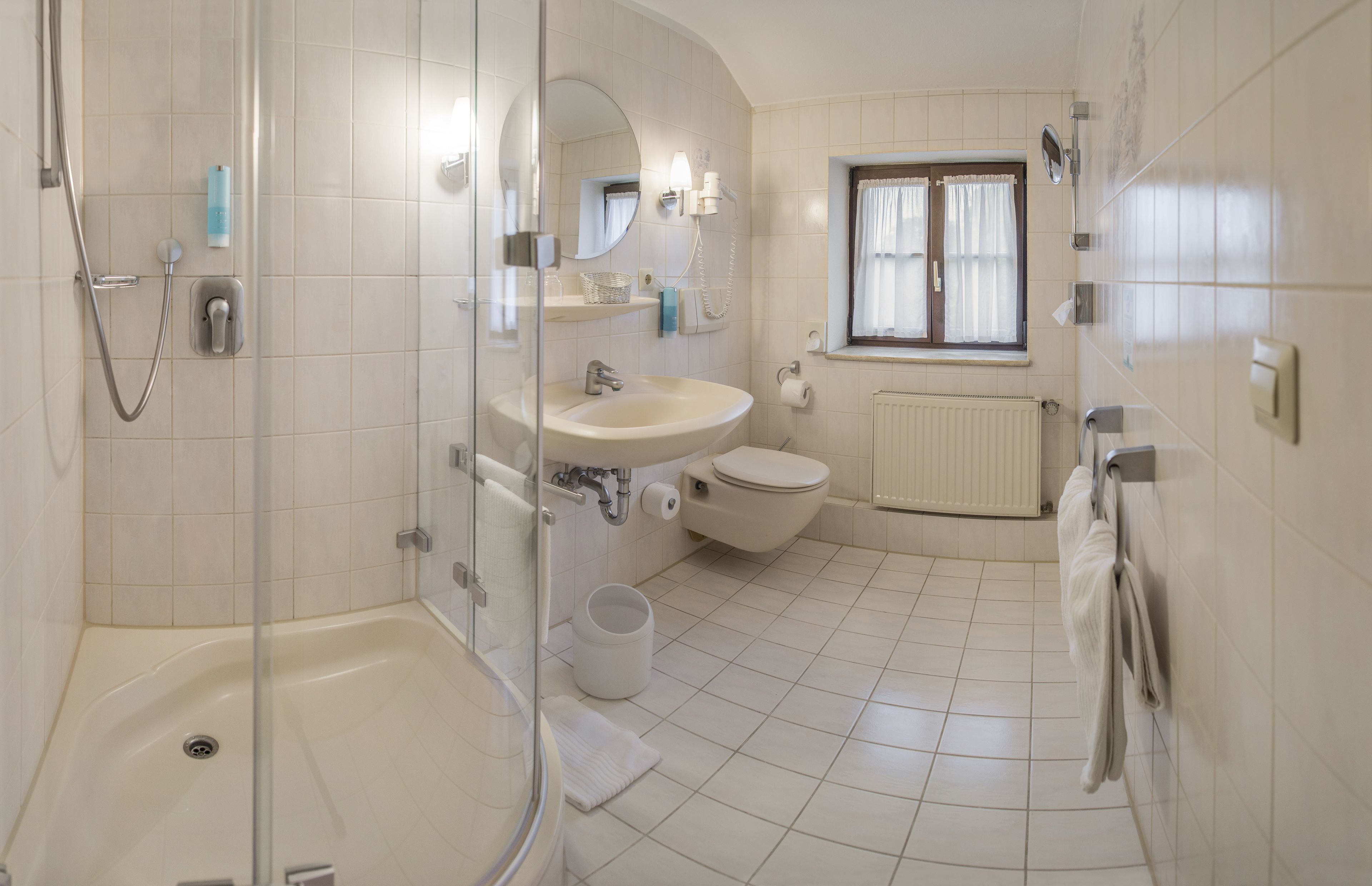 Ein Badezimmer mit Duschkabine, Waschbecken, Toilette und einem Fenster mit Vorhängen.