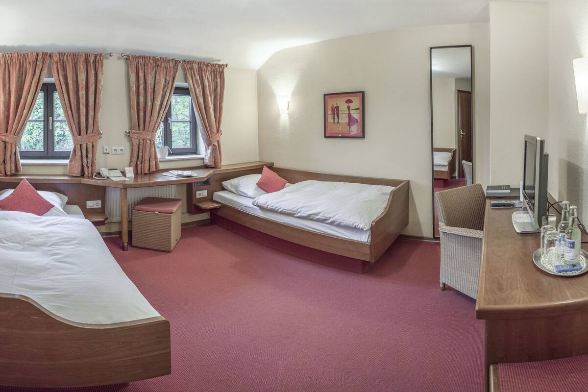 Ein Hotelzimmer mit zwei Betten, einem Schreibtisch, einem Stuhl und einem Spiegel.
