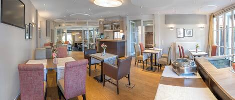 Un moderno vestíbulo de hotel con una zona de bar central, espacios de descanso y vista al comedor.