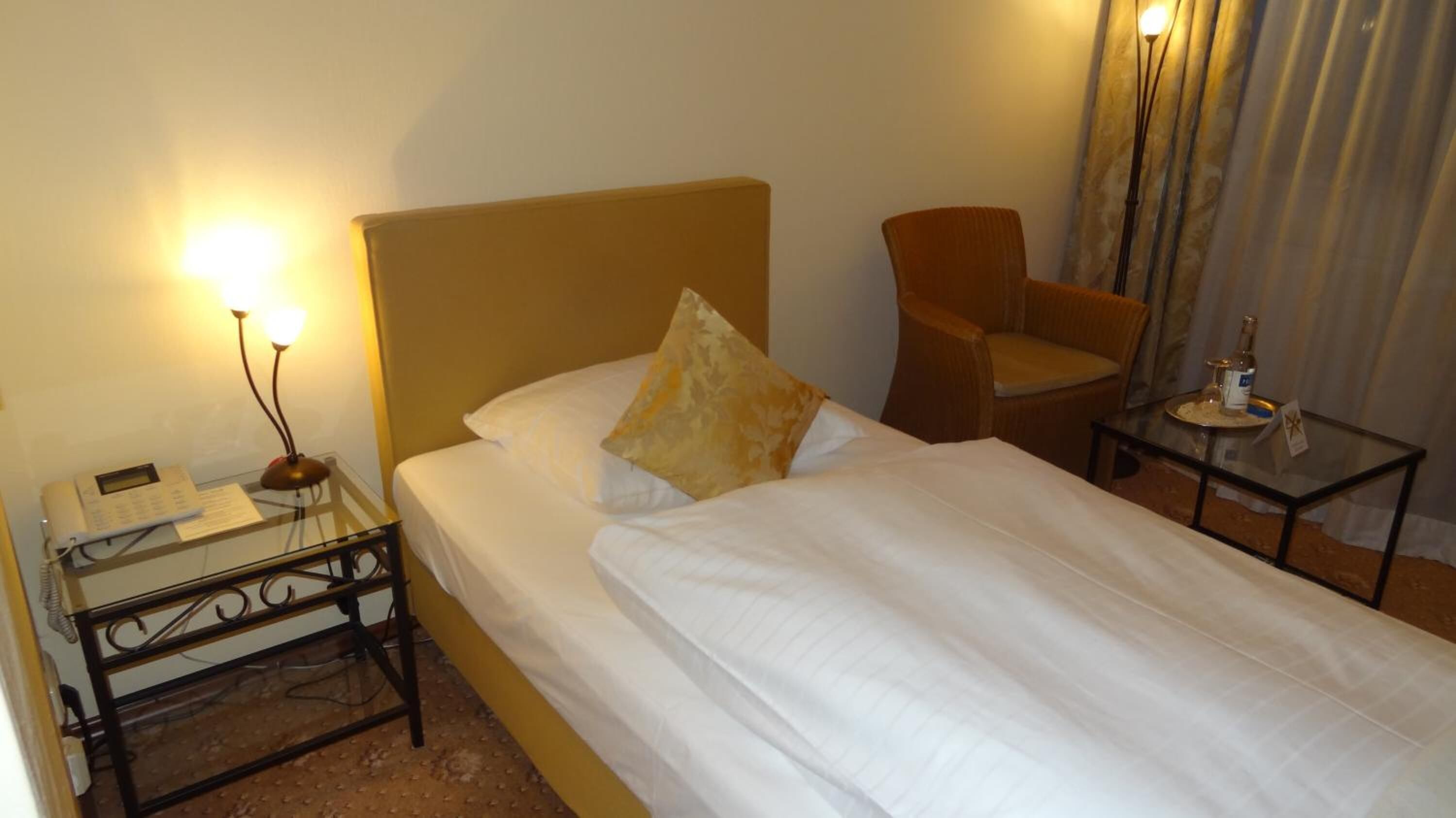 Een hotelkamer met een bed, een stoel, een nachtkastje met een lamp en een telefoon.