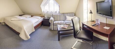 A hotel room with a bed, a sofa, a desk, a chair, a TV, and a window with curtains.