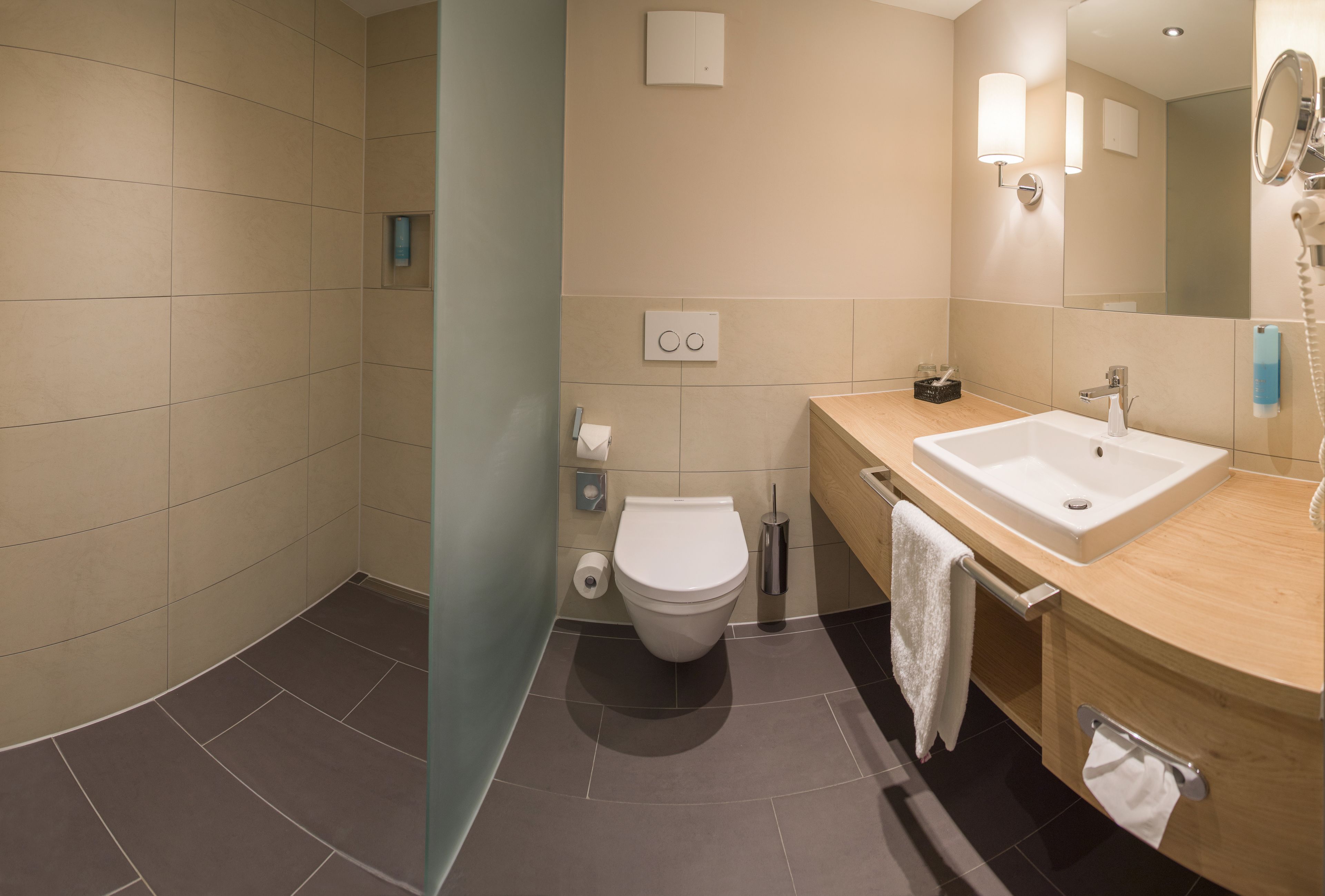 A modern bathroom with a shower, toilet, sink, and mirror.