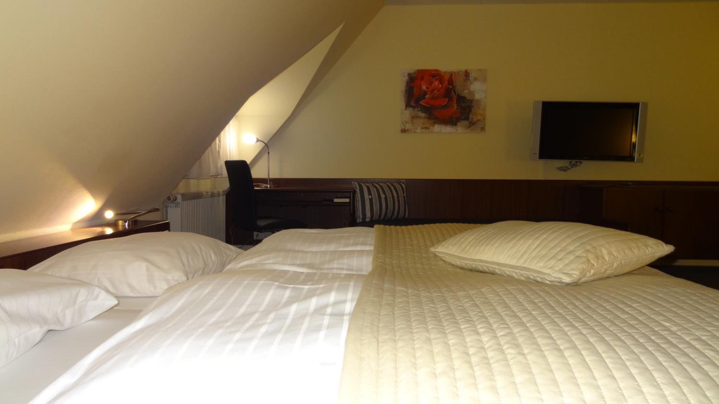 A hotel room with a large bed, a desk, a chair, a flat-screen TV, and a painting on the wall.