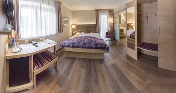 Quarto de hotel com cama, mesa de cabeceira, cadeira, escrivaninha e guarda-roupa.