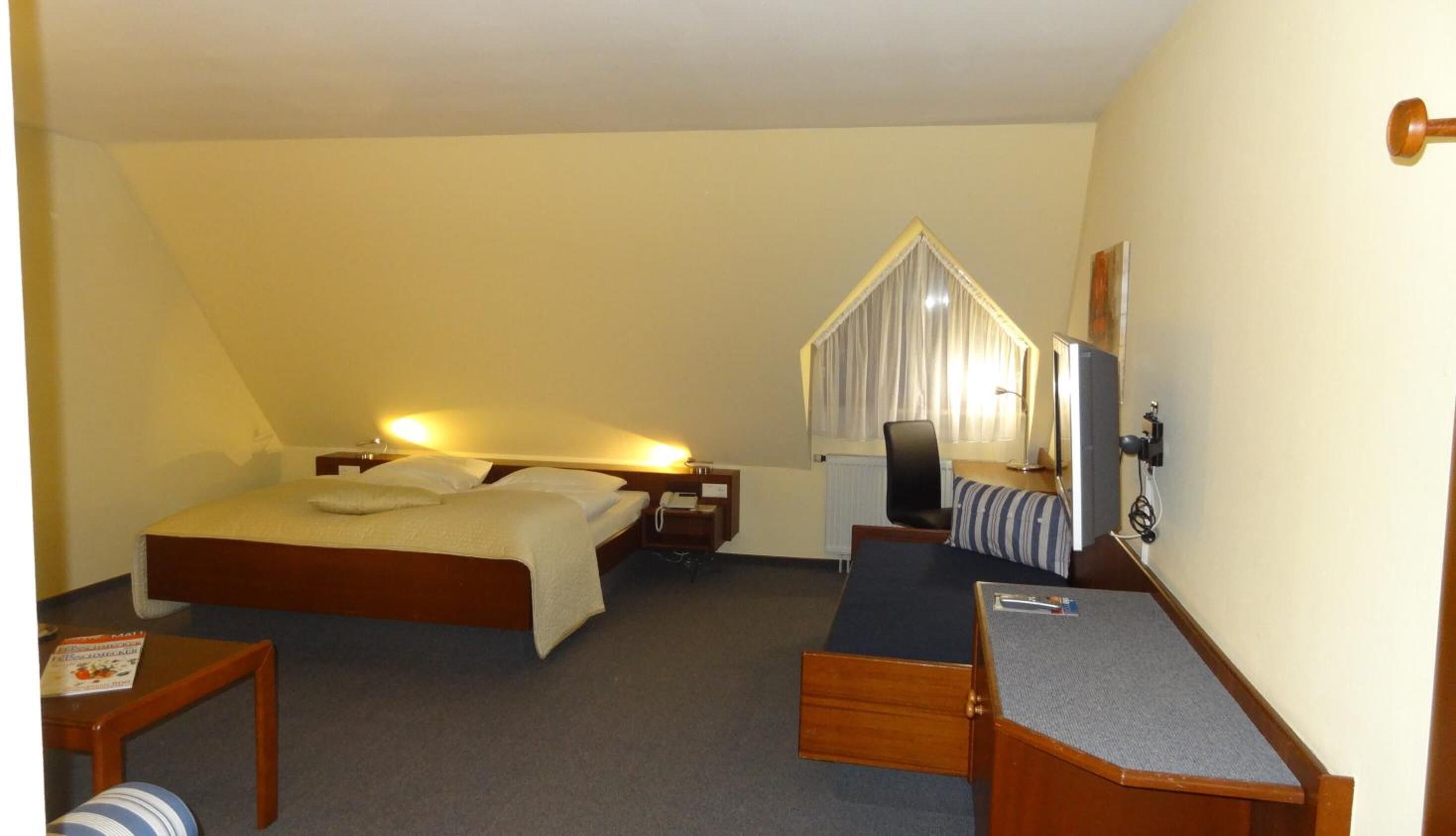 Habitación de hotel con una cama individual, un escritorio con silla, una mesita y un televisor.