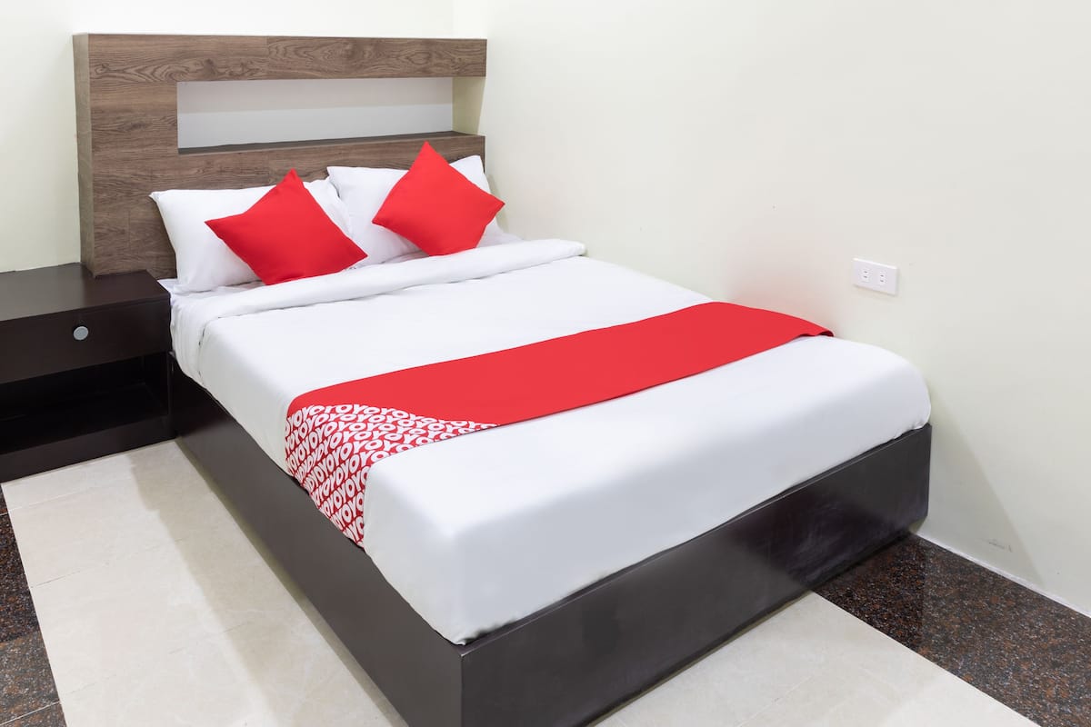 A neatly made bed with white and red bedding, a wooden headboard, and a red throw blanket.