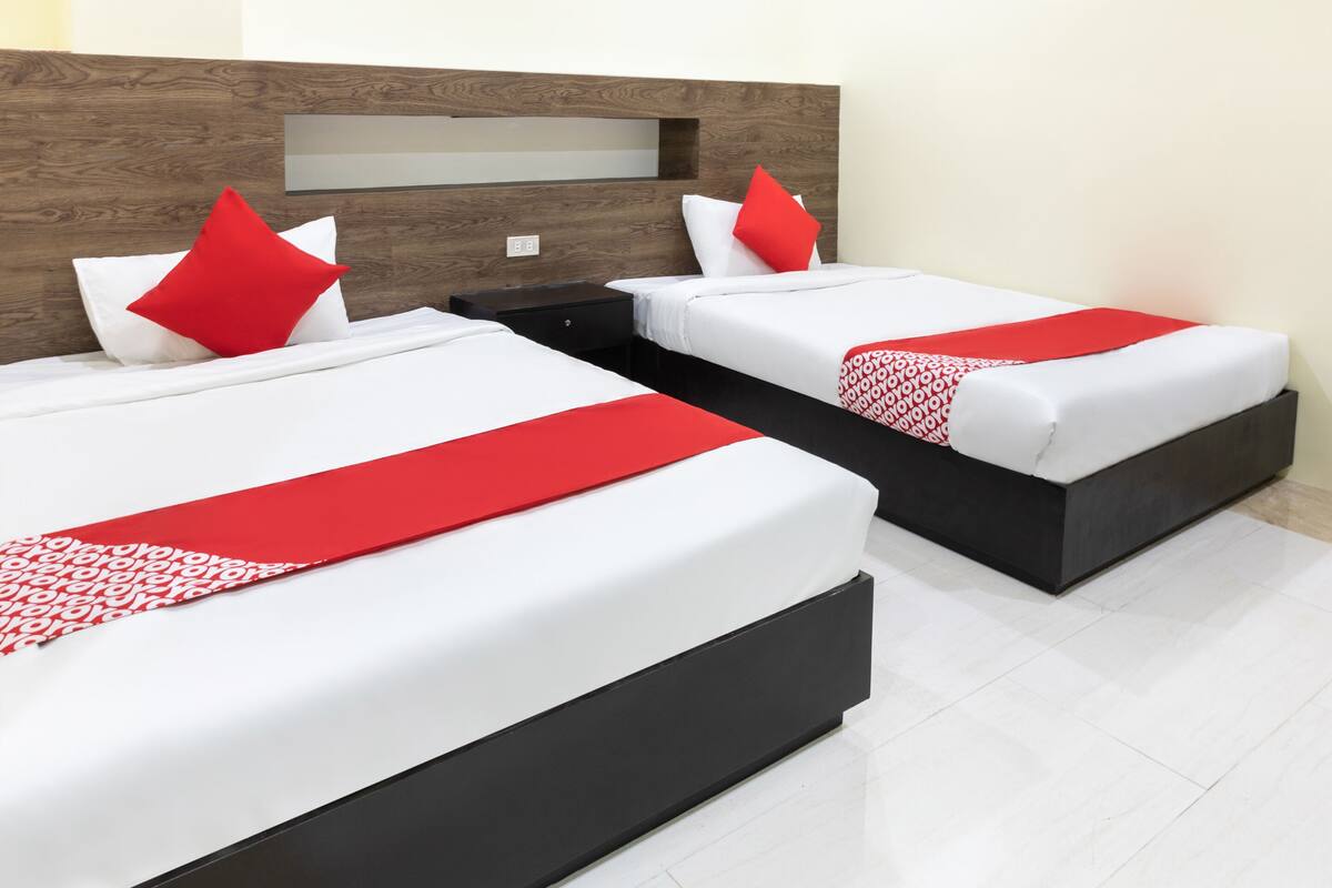 A hotel room with two beds, each with white bedding and red accents, a wooden headboard, and a black nightstand.