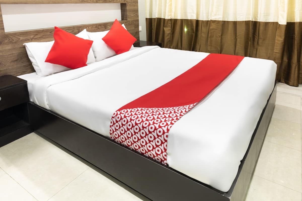 A neatly made bed with white and red bedding, a wooden headboard, and a brown curtain.