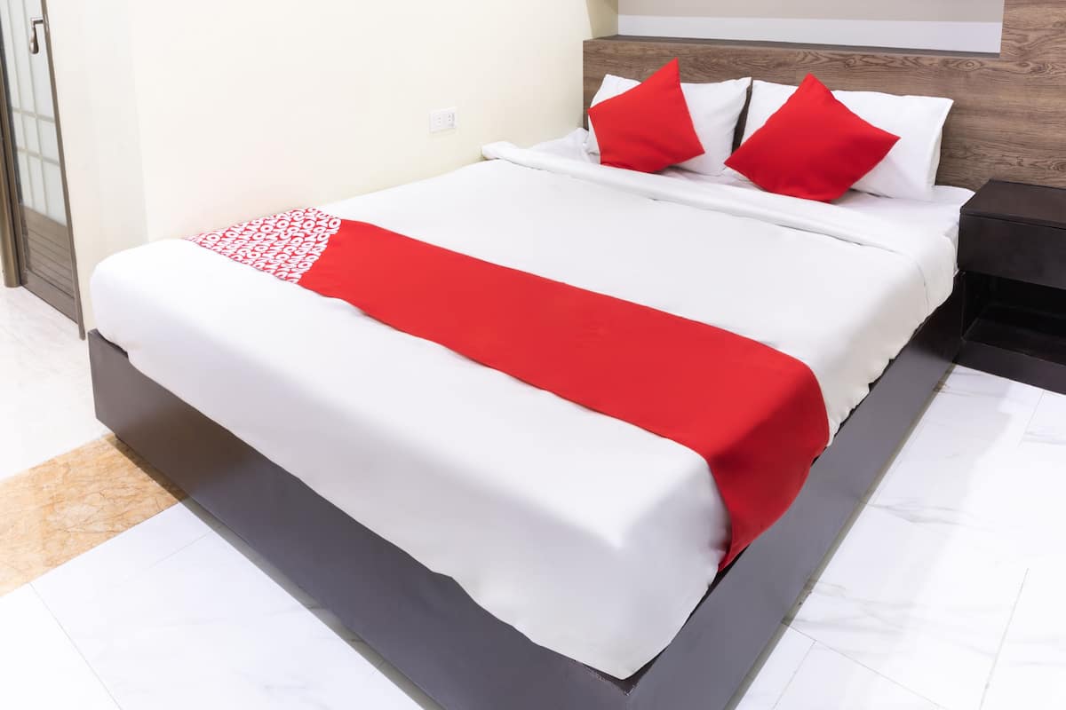 A modern hotel room with a large bed, white bedding, and red accents.