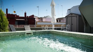 Uma piscina no terraço com água cristalina, rodeada por uma grade de metal e um guarda-sol branco.