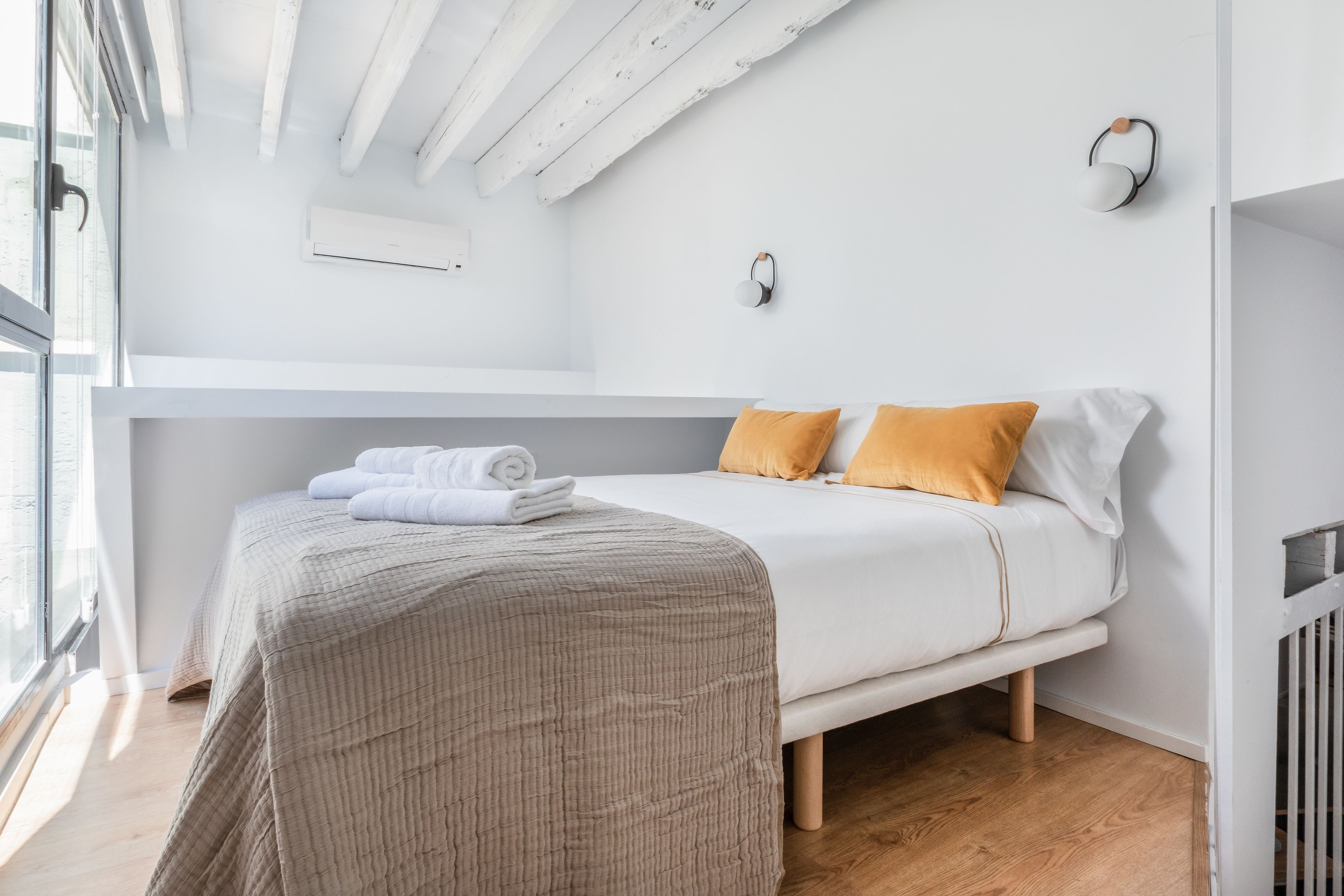 Ein modernes Schlafzimmer mit Bett, Nachttisch, Wandleuchte und Fenster.