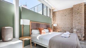 Um quarto moderno com uma cama grande, duas luminárias de cabeceira, uma pequena mesa de madeira e um vaso grande.