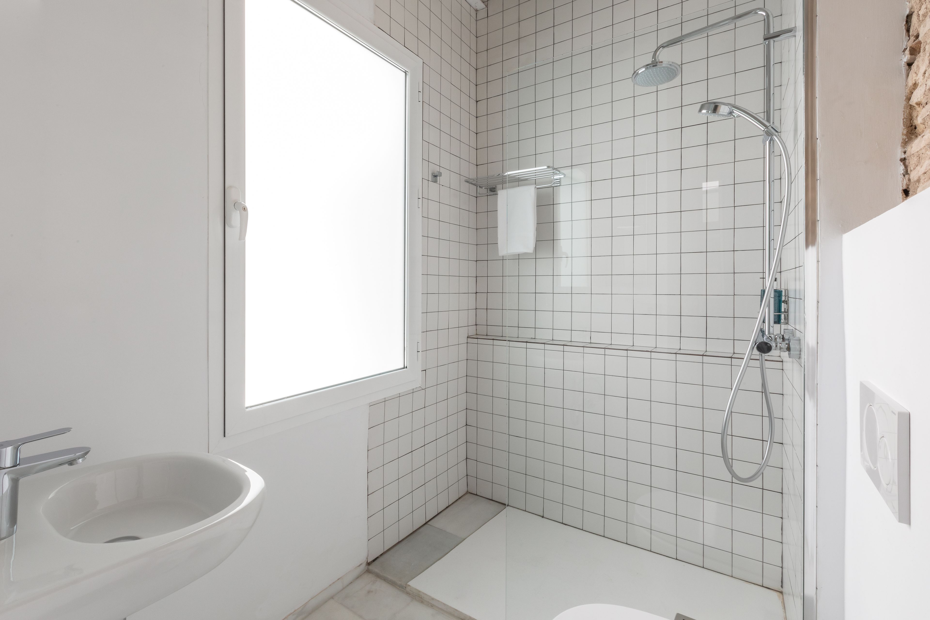 Une salle de bain moderne avec un lavabo blanc, une douche et une fenêtre.