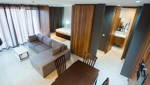 Una sala moderna con un sofá, una mesa de comedor y una mesita de centro. Se ve una cama al fondo y un baño por una puerta abierta.