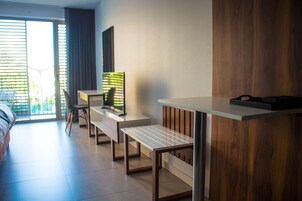 A modern hotel room with a bed, a desk with a chair, a TV, and a large window with blinds.