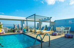 Una piscina al aire libre, sombrillas, sillones reclinables de piscina