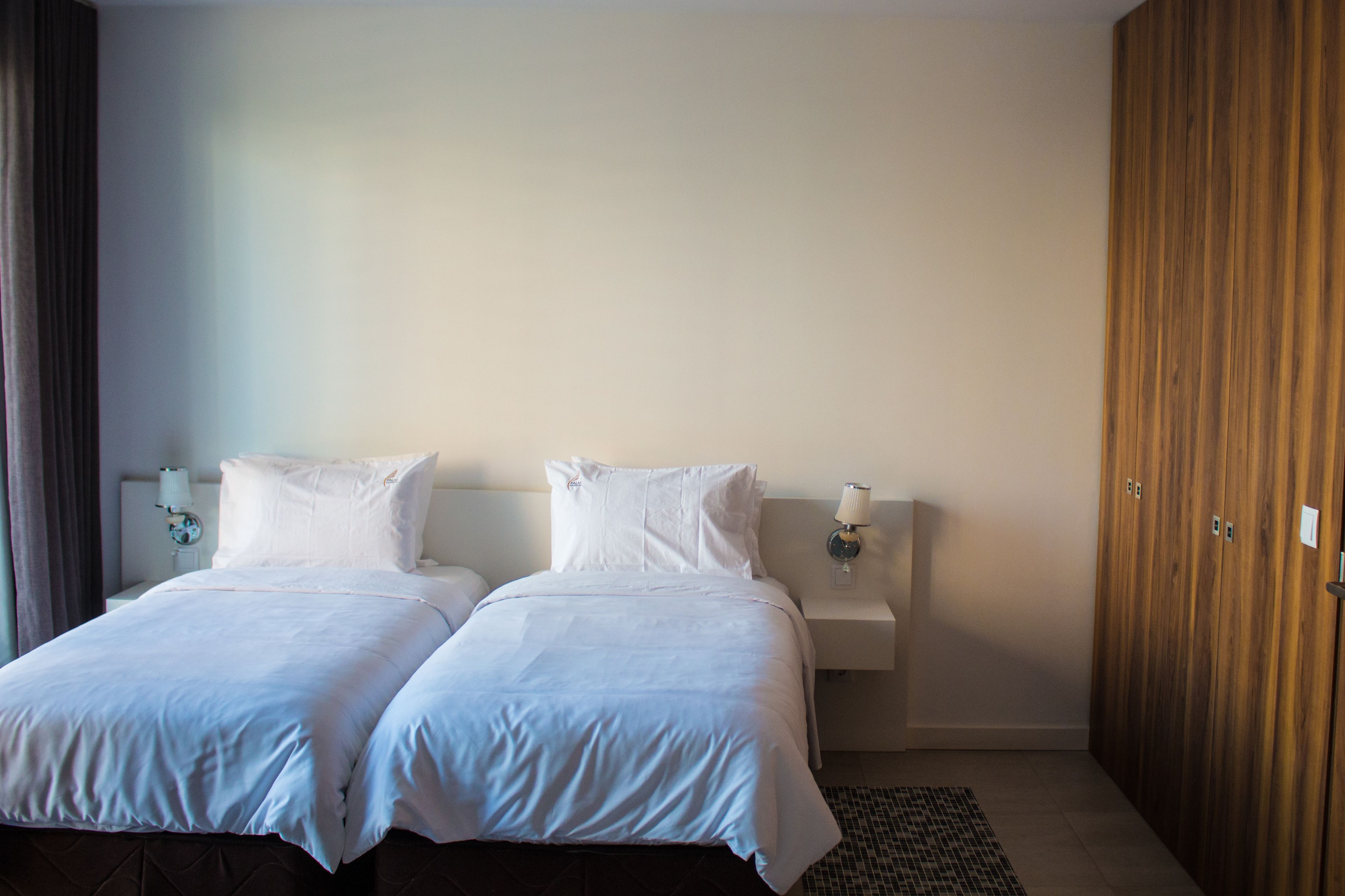 A double bed with white linens, a bedside table with a lamp, and a wooden wardrobe.