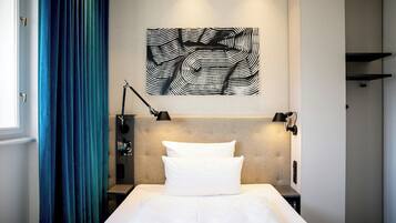 Hotelkamer met een bed, hoofdeinde, wanddecoratie, lamp en raam met gordijnen.