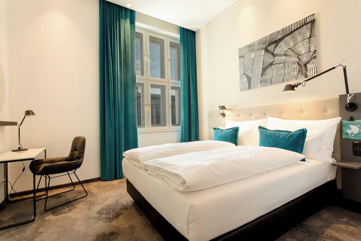 A hotel room with a large bed, a desk, a chair, and a window with curtains.