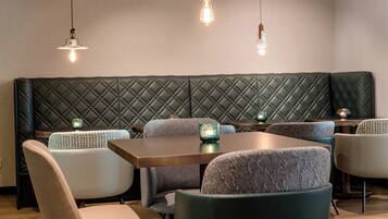 A restaurant interior with a green quilted bench, patterned chairs, and hanging pendant lights.