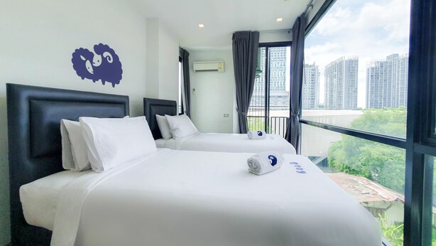 A hotel room with two beds, a large window with a city view, and a decorative wall piece. - Kokotel Bangkok Sukhumvit 50 (Bangkok)