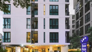 A modern building with a sign for "Kokotel" and a parking area with a white car and a security guard. - Kokotel Bangkok Sukhumvit 50 (Bangkok)