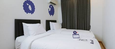 Habitación de hotel con cama doble, ropa de cama blanca, cabecera oscura y aire acondicionado de pared.