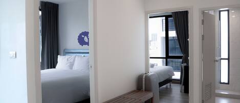 Una habitación de hotel moderna con cama, un banco, una maleta y vistas a la ciudad a través de la ventana.